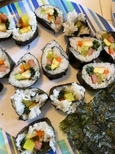 photo of homemade kimbap on a striped plate with a piece of roasted seaweed on the side