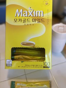 Box of Korean Maxim mocha instant coffee and an individual packet next to it with a pink travel mug on the side